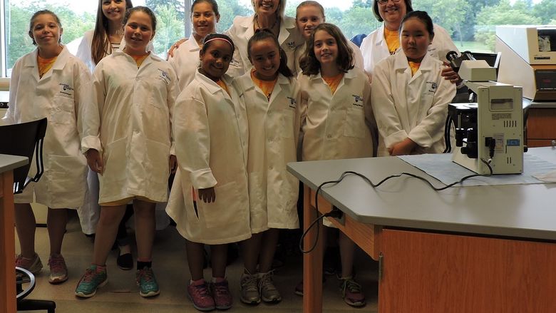 group of young girls in lab coats pose with professors