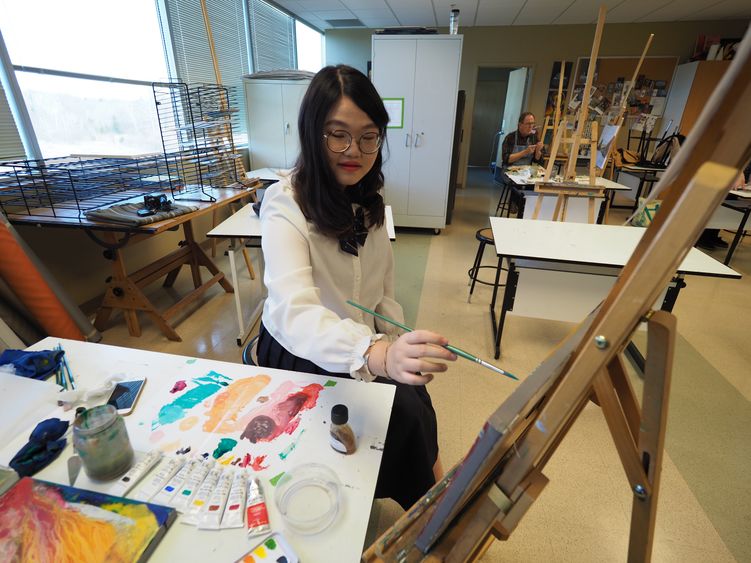 a female student sits in front of an easel