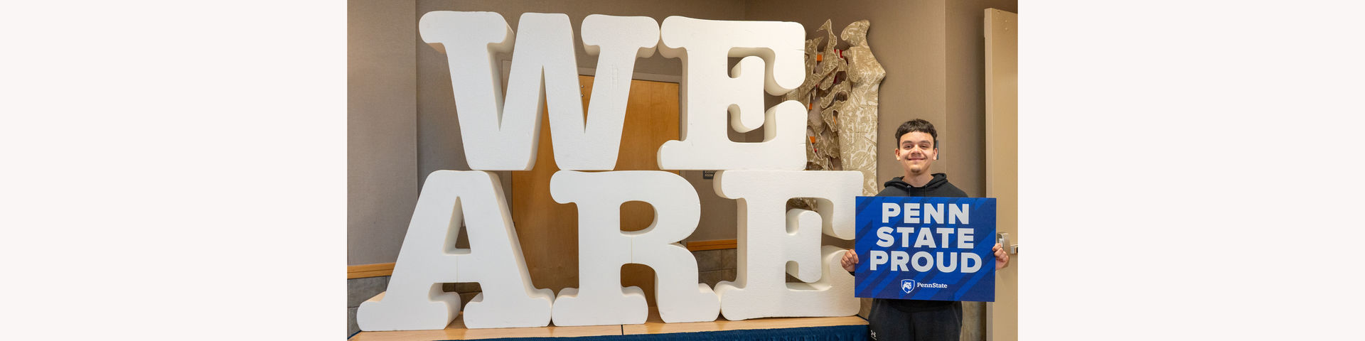 Student smiling at camera in front of letters WE ARE