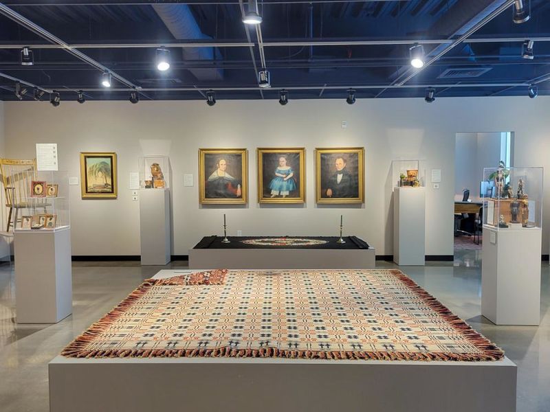 A gallery with classical paintings on the wall and textiles laid out for display throughout the room