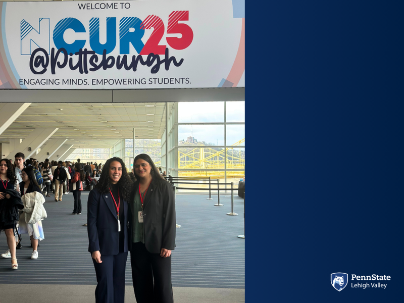 two female students smile in front of a conference banner