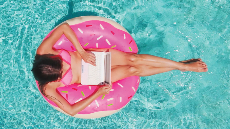 Woman with a laptop in bathing suit sitting in pink round float in a pool