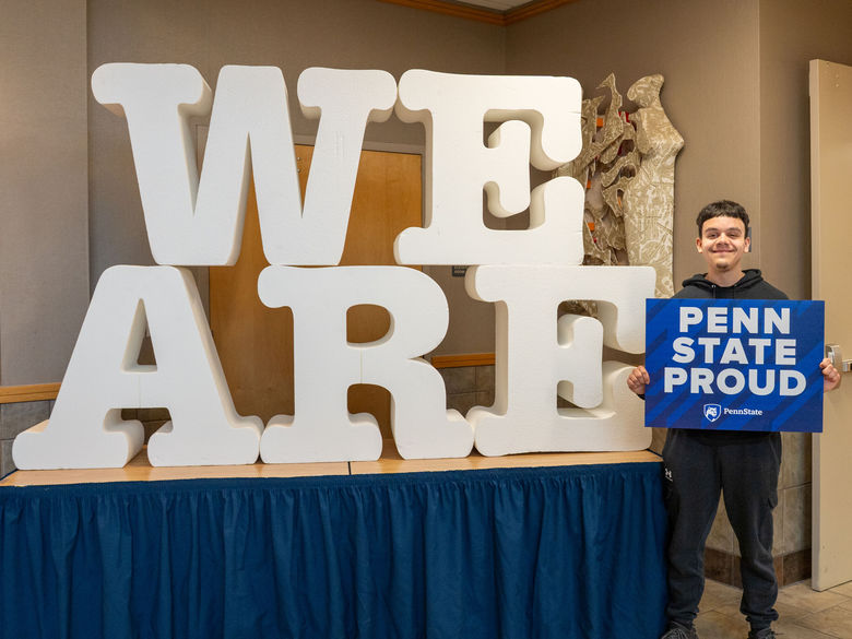 male student holding a Penn State Proud sign next to words WE ARE 