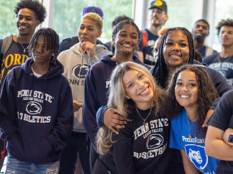 Group of students indoors, many wearing Penn State Lehigh Valley apparel, standing in front of large windows with greenery visible outside.