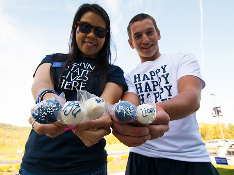penn state alumni holding PSU-themed cake pops and smiling at the camera in their penn state gear