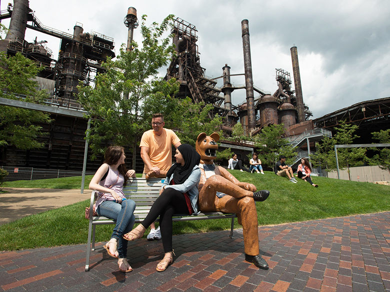 students hanging out in front of the steel stacks on the nittany lion bench