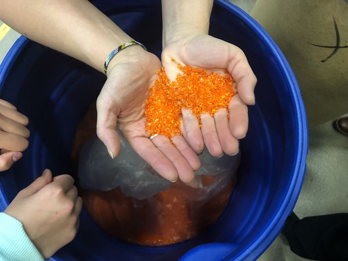 hands hold orange plastic particles
