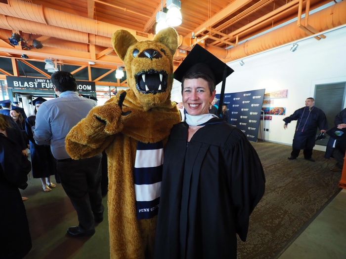 Nittany Lion posing with woman in cap and gown