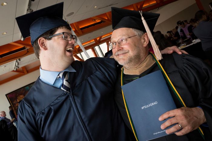 Graduate in cap and gown with a faculty member smiling at each other