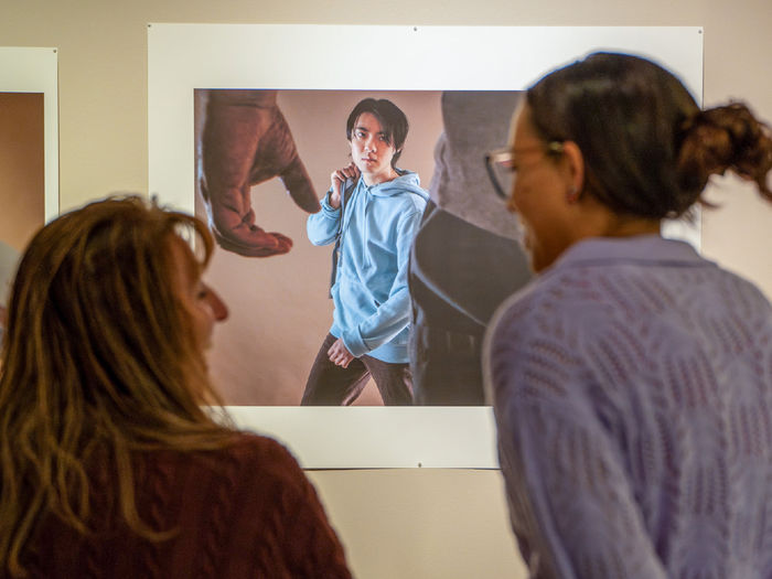 Two women talk in the foreground of an image, in front of a print photo of a boy looking up at a camera.