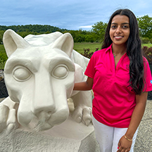 PSU-LV female student in bright pink New Student Orientation leader shirt smiling, standing next to the PSU-LV lion shrine.