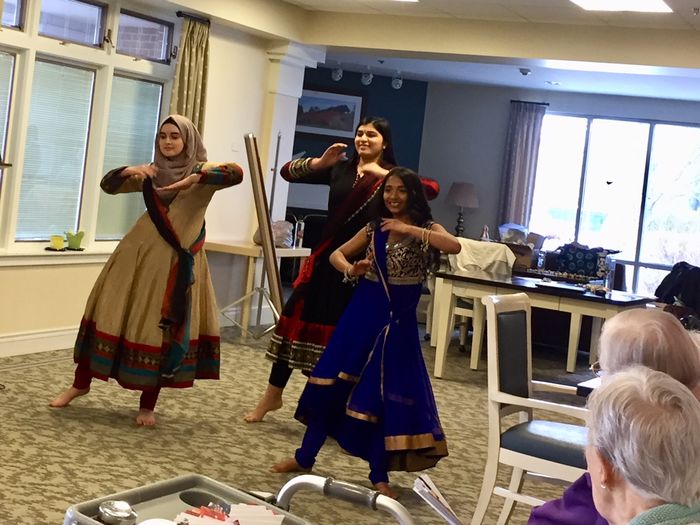 three young women in cultural dress dancing at senior center