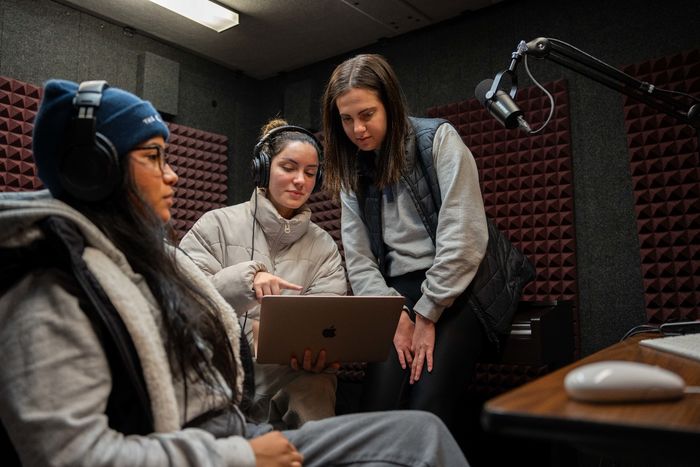 3 female college students sit in a podcasting booth 