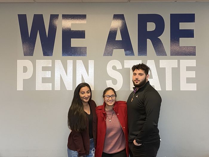 three students in front of a We Are Penn State 