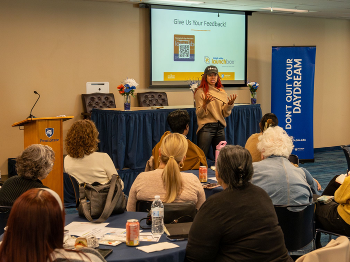 a woman speaks in front of an audience seated at round tables