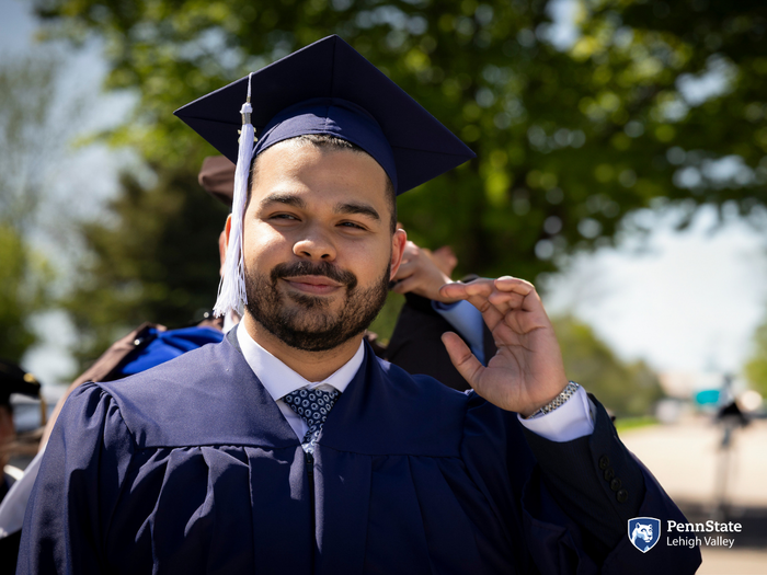 a male student in blue regalia smiles as he prepares to process in a commencement ceremony