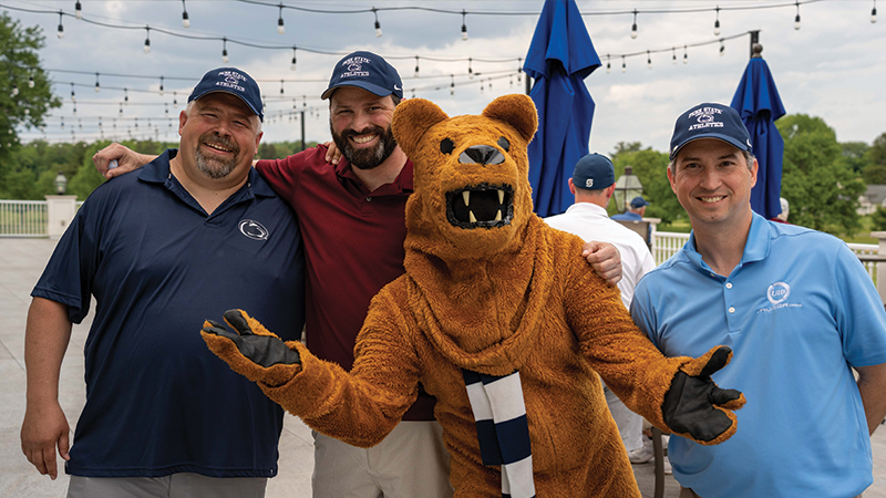 Three male golfers stand with the Nittany Lion mascot