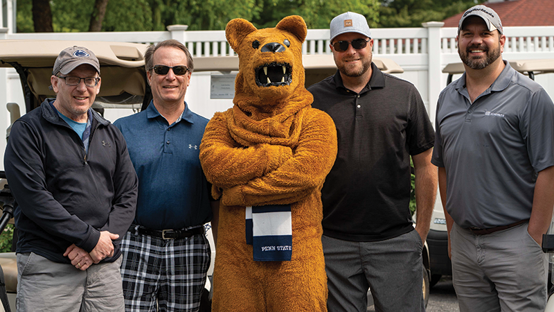Four male golfers stand with the Nittany Lion mascot.