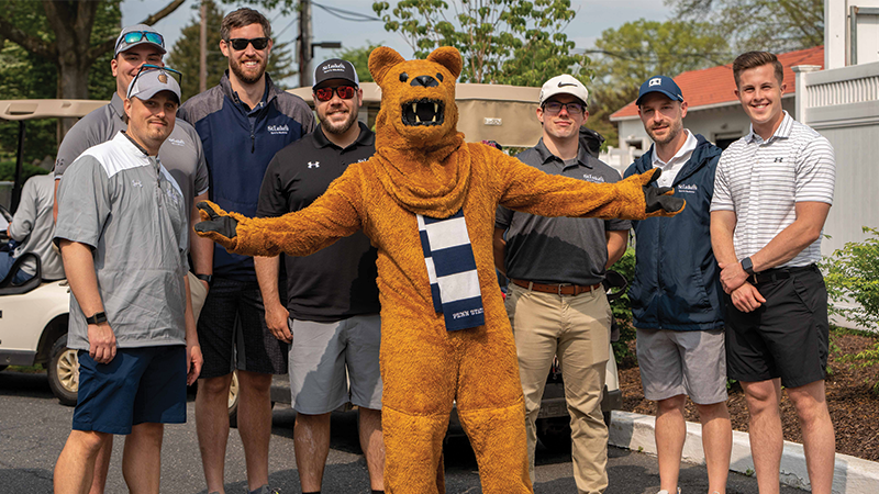 Seven male golfers stand with the Nittany Lion mascot.