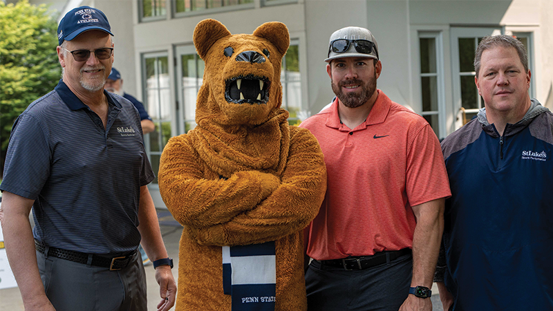 Three male golfers standing with the Nittany Lion mascot.