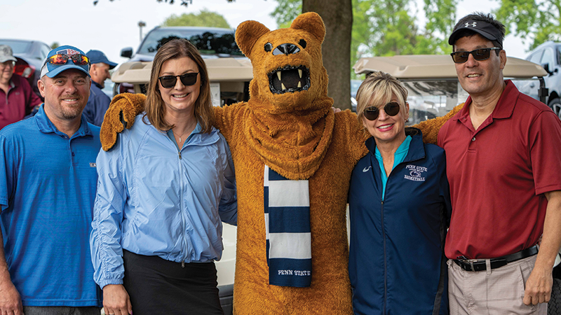 Four golfers, two male and two female, stand next to the Nittany Lion mascot.