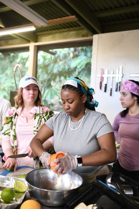 A student wearing a gray shirt and colorful headband prepares food in a kitchen