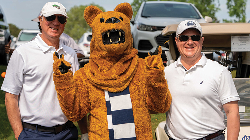 Two male golfers stand beside the Nittany Lion mascot 