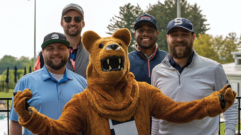Three male golfers stand next to the Nittany Lion mascot
