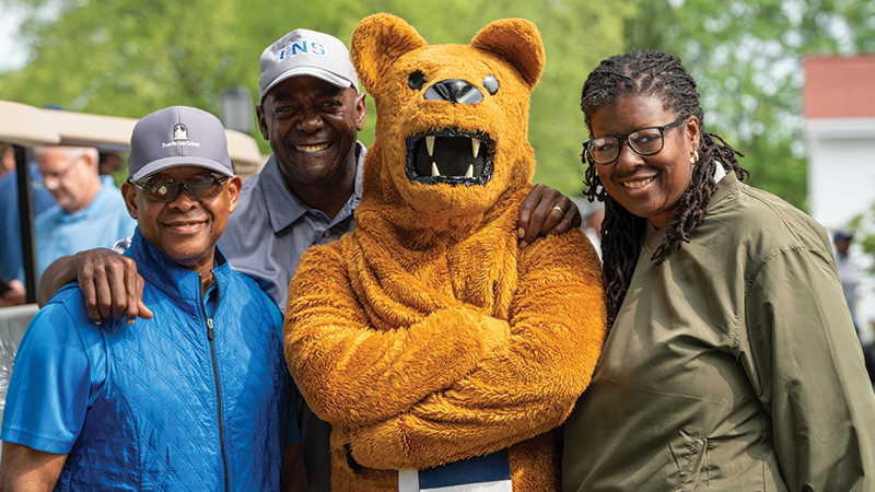 Three golfers stand around the Nittany Lion mascot.