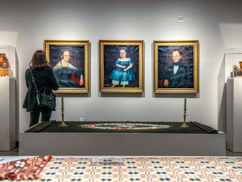 A woman stands in front of a series of three portraits