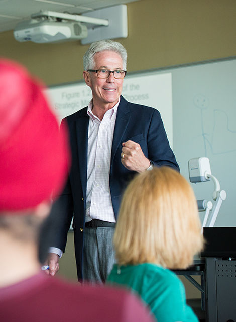 A male instructor in a classroom standing in front of his students lecturing in an engaging manner.