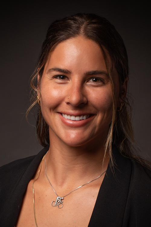 Woman with long brown hair looks at camera and smiles. 
