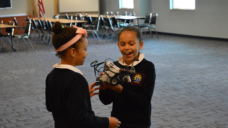Two female students play with a LEGO robot