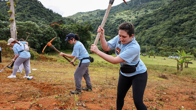 A student actively swings a tool while planting kidney beans in Puerto Rico