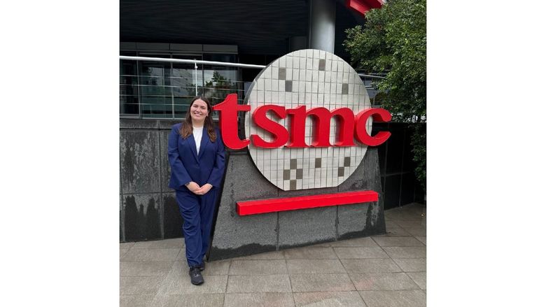 A student stands in front of a company sign that reads "tsmc"