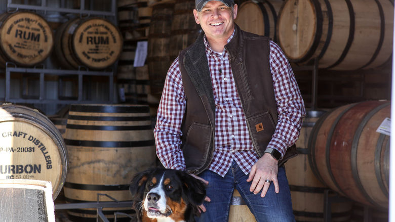 photo of man in vest with dog surrounded by barrels