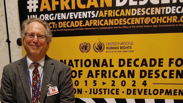 David Livert stands in front of a sign at the Permanent Forum of People of African Descent in Geneva  