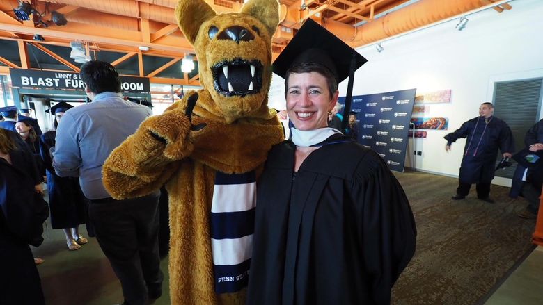 Nittany Lion posing with woman in cap and gown