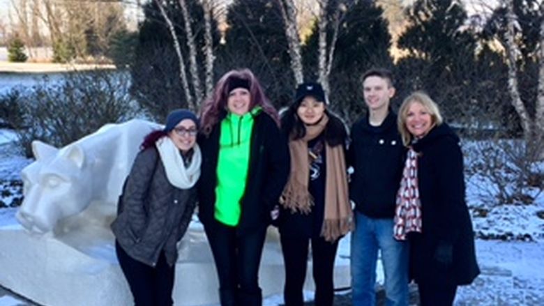 Four students and professor in front of lion shrine