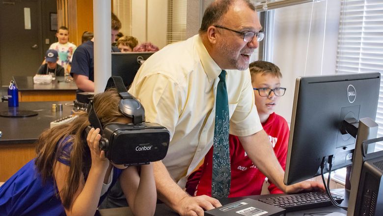 Michael Gallis assists middle schoolers who are trying on VR headsets.