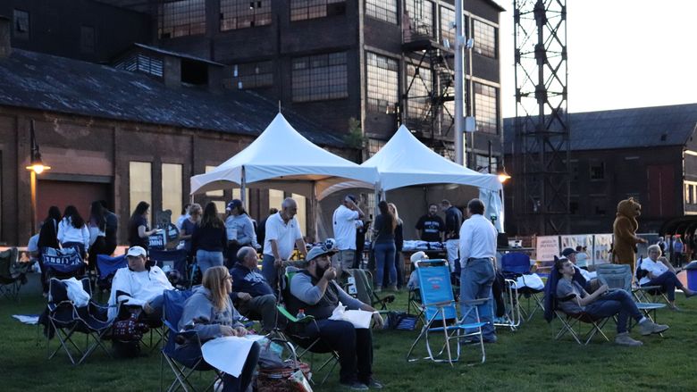 group of people sitting on lawn ready to watch big screen