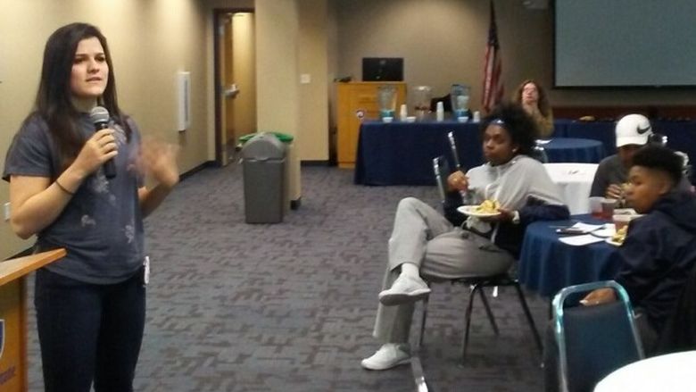 A guest speaker holding a microphone speaks to room full of students