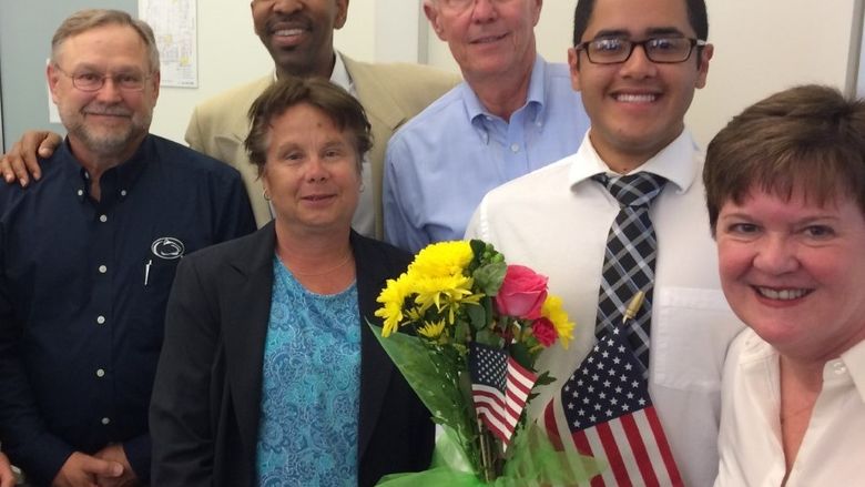 six adults smiling and posing with american flag and flowers