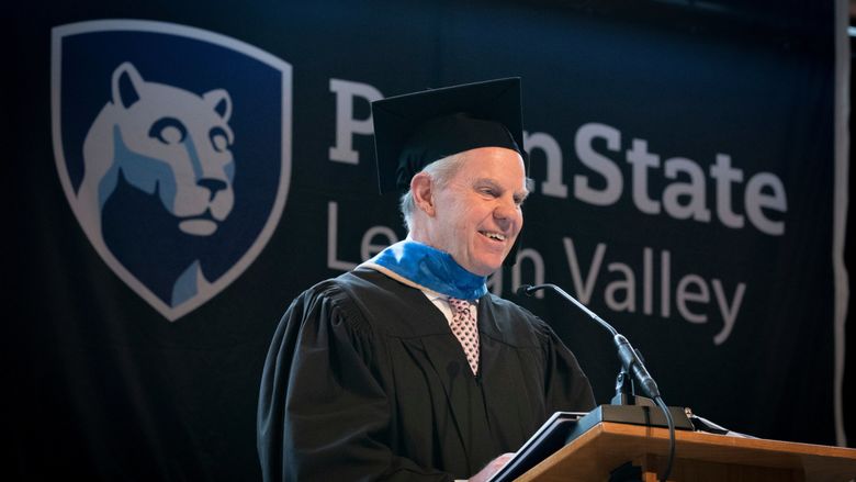 man in cap and gown delivering remarks at podium