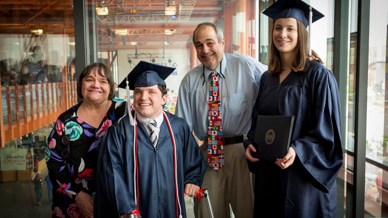 four people standing and smiling, two in caps and gowns