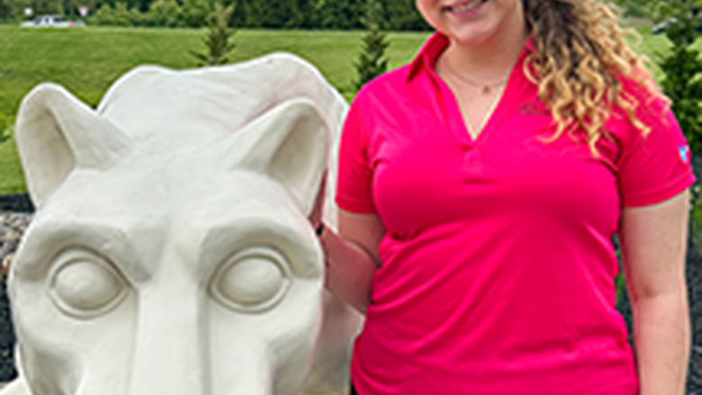 PSU-LV female student in bright pink New Student Orientation leader shirt smiling, standing next to the PSU-LV lion shrine.