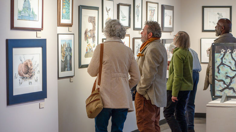 A group of people stand in front of a gallery wall and admire the arranged art pieces