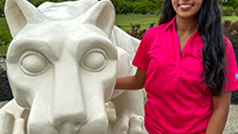 PSU-LV female student in bright pink New Student Orientation leader shirt smiling, standing next to the PSU-LV lion shrine.