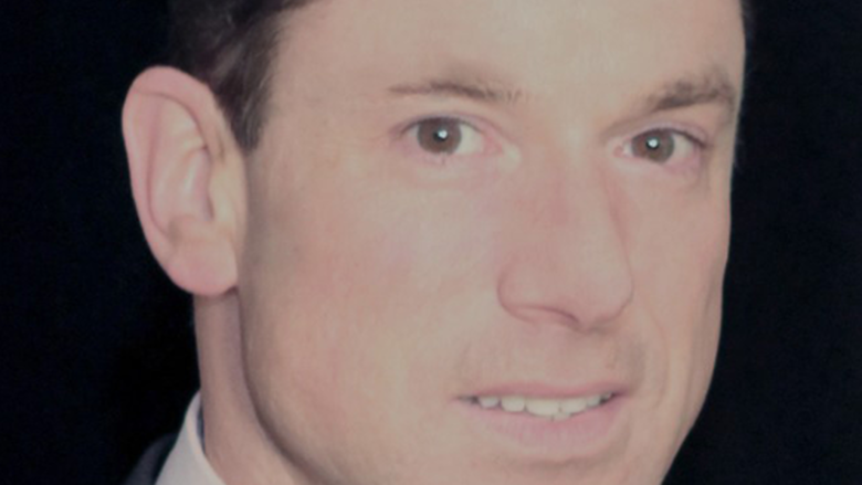 Man looking at camera, wearing a suit and light blue bowtie.