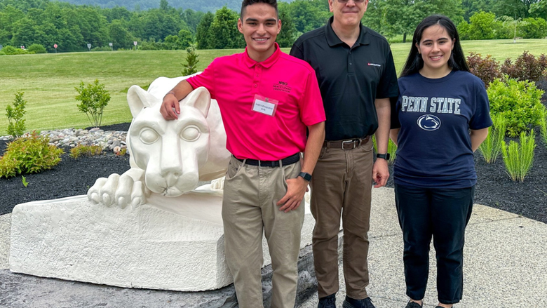 3 adults smile in front of a lion shrine 
